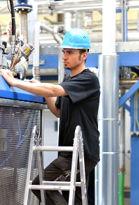 Industrial worker in a hard hat operating machinery while standing on a ladder