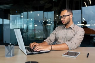 Man in glasses working on laptop at modern office desk