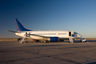 Commercial airplane parked on tarmac at sunset with boarding stairs and clear sky