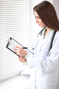  female doctor in white lab coat and stethescope updating patient chart