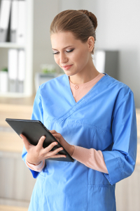Female healthcare professional in blue scrubs using a tablet computer.