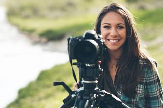 Smiling female photographer with DSLR camera on a tripod outdoors by a river