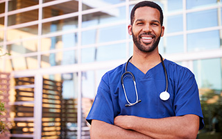 Confident male nurse in blue scrubs with stethoscope standing outside a medical building