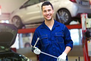 Male mechanic in blue overalls holding a wrench in a car repair shop with a car in the background