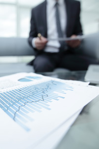 Businessman in suit sitting with tablet reviewing financial graphs on paperwork in an office setting