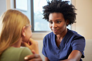 Nurse in blue scrubs consulting with patient in medical office setting.