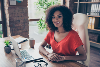 Woman with curly hair sitting at a desk with a laptop in a cozy office space.