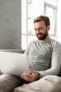 Man with beard using laptop while sitting on a couch in a well-lit room