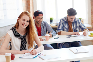 Three college students studying and working on projects in a bright classroom.