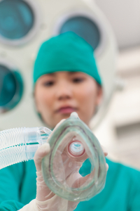 Anesthesiologist in scrubs holding a breathing mask in an operating room.