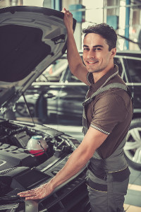 Male mechanic standing by a car with open hood in a workshop