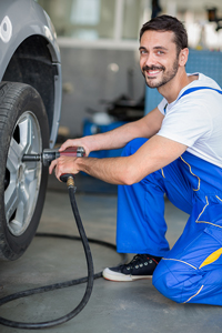 Smiling mechanic in blue overalls using an air wrench to change a tire in an auto repair shop