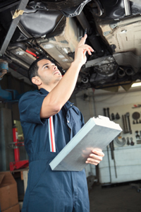 male auto mechanic in blue coveralls under a car