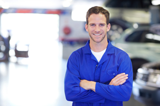 Smiling mechanic in blue uniform standing with arms crossed in a car repair shop.