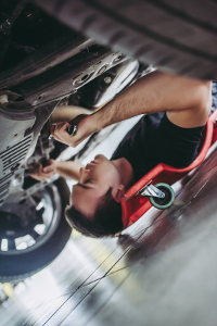 Man lying on a creeper under a car, using a wrench to work on the underside of the vehicle in a garage.