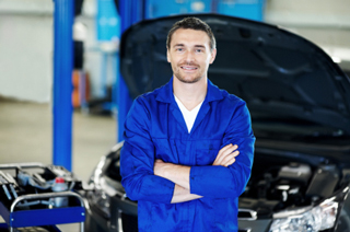 Auto mechanic with his arms crossed standing in front of a car with the hood up.