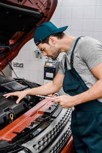 Mechanic in overalls and cap checking car engine in workshop