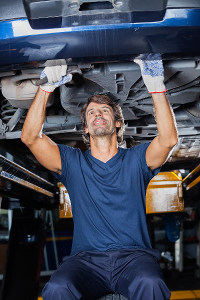 Mechanic working under car, tightening bolts on vehicle's undercarriage in a workshop