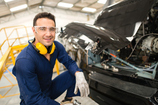 Mechanic in blue jumpsuit and safety glasses repairing a car engine in a workshop