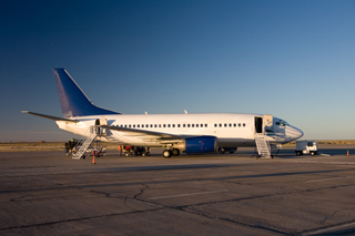 Commercial airplane parked at airport terminal during sunrise with boarding stairs attached to the open cabin door.
