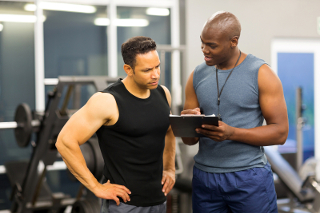 Fitness trainer and client discussing workout plan on a digital tablet in a gym.