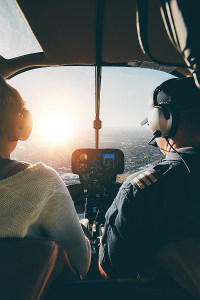 Two people in a helicopter cockpit enjoying a scenic flight at sunset.