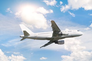 Commercial airplane flying under blue sky with clouds and bright sunlight