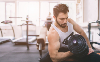 Man lifting dumbbell in gym, focused on exercise with gym equipment in background