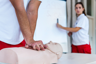 CPR training session with one instructor demonstrating on a mannequin and the other instructor writing on a whiteboard in the background