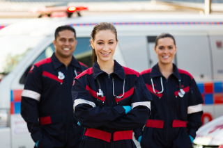 Three paramedics standing in front of an ambulance, smiling, with medical equipment visible