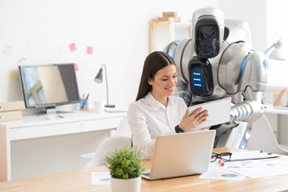 Woman working with advanced humanoid robot at an office desk, showing digital tablet to robot.