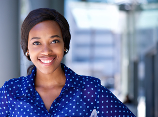 Confident businesswoman smiling in a blue polka dot blouse, standing in an office environment.