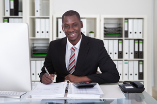 Professional man in suit smiling at desk with paperwork in a well-organized office environment