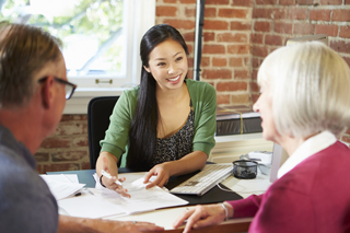 Businesswoman discussing documents with elderly couple in office setting.