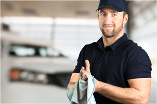 Mechanic in black shirt and cap smiling while wiping hands with a rag in a garage
