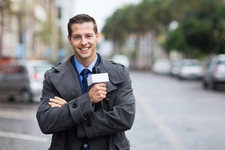 Male reporter holding a microphone on a city street