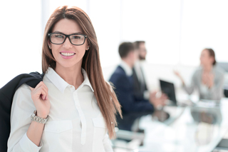 Smiling professional businesswoman with glasses holding jacket in office setting with colleagues in the background