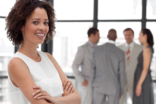 Confident businesswoman with curly hair smiling in office, with colleagues in background.