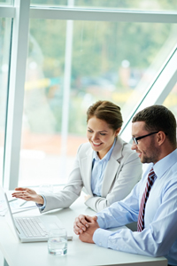 Two professional colleagues collaborating on a laptop in a bright office space.