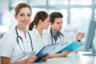 Three medical professionals reviewing data on a computer screen in a hospital setting.