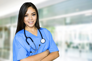 Nurse in blue scrubs with a stethoscope standing in a hospital corridor.