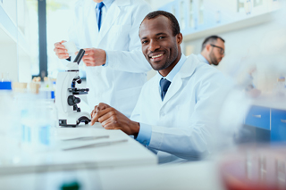 Male scientist using a microscope in a laboratory with colleagues in the background.