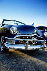 Low angle view of a classic blue 1950s American car with chrome details and clear blue sky in the background.