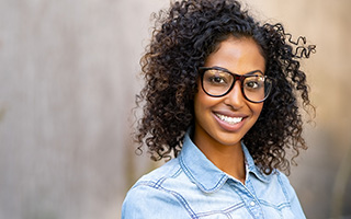 Young woman with dark curly hair and glasses smiling at the camera