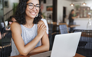 Smiling young woman sitting in front of an open laptop in a room with many tables and chairs