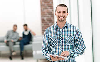 Man holding a tablet in an office environment with colleagues in the background