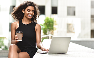 Woman with curly hair using laptop and holding coffee cup while sitting at a counter in a modern professional setting.