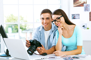 Two photographers reviewing images on a laptop in a bright office setting.