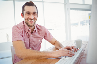 Man in pink shirt using computer at bright office desk