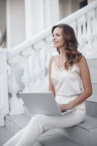 Woman in white outfit sitting on stairs using laptop